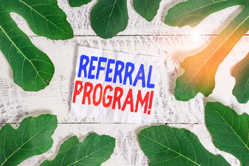 Text sign showing Referral Program. Business photo showcasing internal recruitment method employed by organizations Leaves surrounding notepaper above a classic wooden table as the background