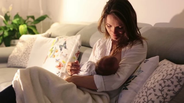 Young beautiful mother, breastfeeding her newborn baby boy at night