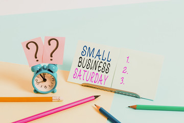 Writing note showing Small Business Saturday. Business concept for American shopping holiday held during the Saturday Mini size alarm clock beside stationary on pastel backdrop