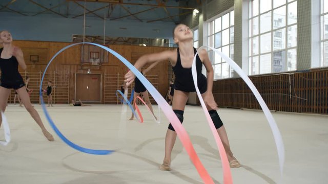 Group of active teenage girls rehearsing rhythmic gymnastics dance together and using ribbons