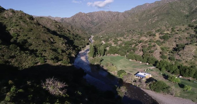 Aerial traveling along clean rocky river valley towards panoramic view of mountain chain. Wild forest landscape. Rio grande, Nogoli, San Luis, Argentina