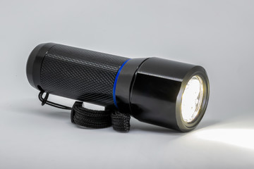 A black metal flashlight on its side, powered on, isolated on a white background.