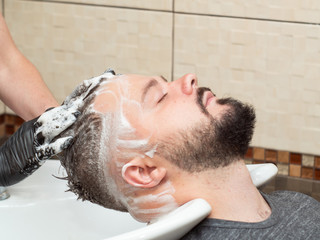 Obraz premium Stylist shampoo males hair in wash stand, close up view. Hairdressers hands in black rubber gloves. Male in barbershop. Selective soft focus. Blurred background