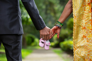 Indian couple holding hands and baby shoes 