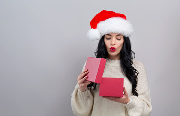 Young woman with santa hat opening a Christmas gift box on a gray background