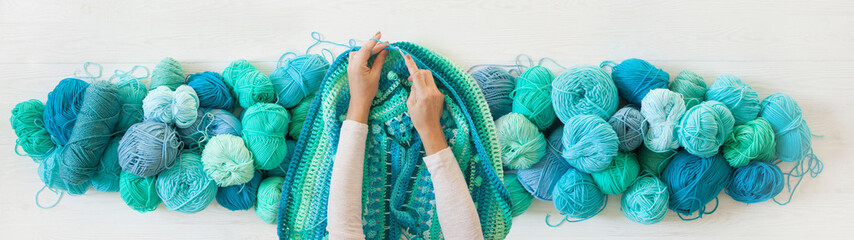 Women's hands are large. Woman crochets. Yarn of green, turquoise, aquamarine and blue colors....