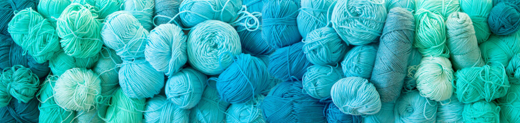 Yarn of green, turquoise, aquamarine and blue colors. White wood background. Knitting needles and...