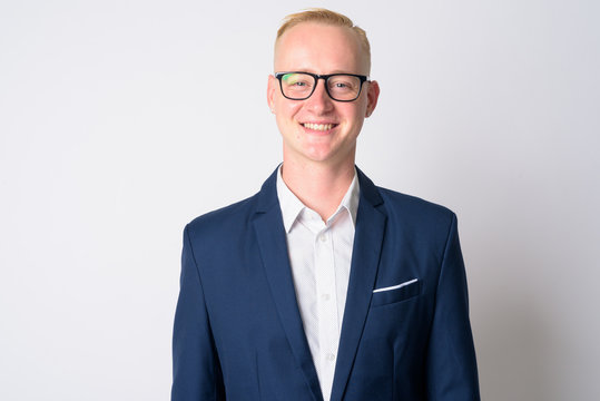 Face of happy young blonde businessman in suit smiling and wearing eyeglasses
