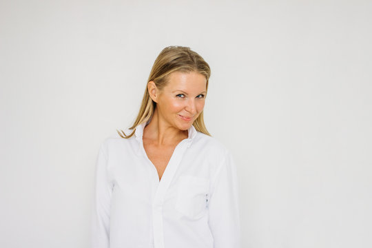Portrait of flirting blonde forty year woman with long hair in white shirt on white wall background isolated