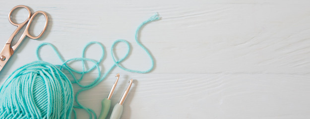 Yarn of green, turquoise, aquamarine and blue colors. White wood background. Knitting needles and crochet hooks. Scissors. White long background.