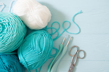 Yarn of green, turquoise, aquamarine and blue colors. White wood background. Knitting needles and...
