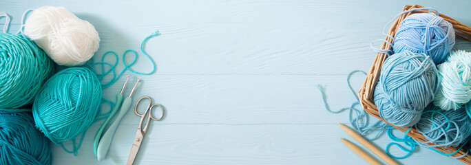 Yarn of green, turquoise, aquamarine and blue colors. White wood background. Knitting needles and crochet hooks. Scissors. Blue long background.