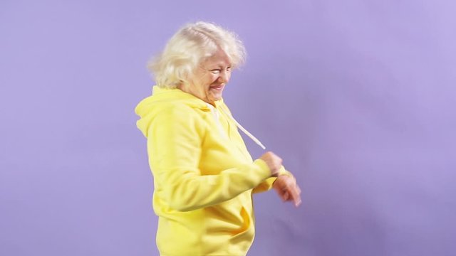Stylish granny in a yellow sports sweatshirt moving to music, dancing party, style. Slow motion