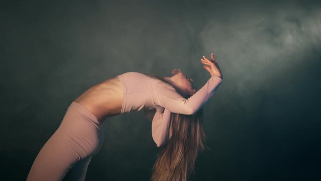 Portrait of beautiful girl in pink tight-fitting suit sensually dancing in dark studio with purple lamps.Concept of choreography, dance, performance