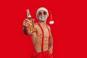 Christmas Freestyle. Young bearded Santa Claus bare muscular upper body in hat standing isolated on...