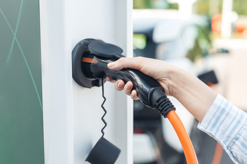 Young adult woman holding power cable supply for charging electric car
