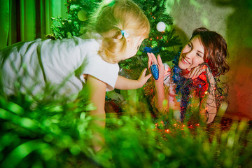 Nice mother and her cute daughter near Christmas tree in the room