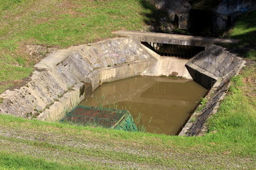 Concrete water reservoir with metal protection bars used to store and filter excessive rainwater during heavy rains surrounded with freshly cut grass on warm sunny summer day