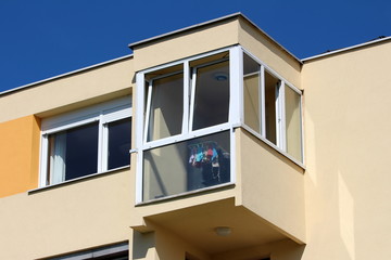 Corner balcony with large glass surface on top of colorful renovated apartment building on warm sunny summer day