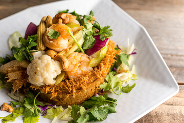 Sauteed shrimp, cashew nuts, cauliflower, corn, and mixed vegetables in a nest made of fried taro. Plated and served on a reclaimed wood table.