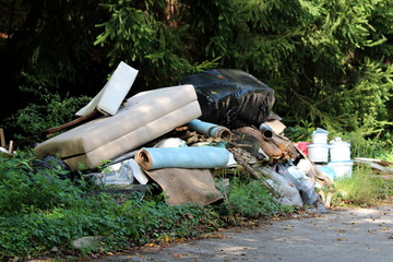 Illegal garbage dump near local paved forest road filled with domestic garbage surrounded with tall...