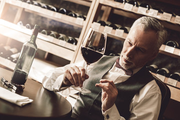 Sommelier Concept. Senior man sitting at table checking quality of red wine pensive