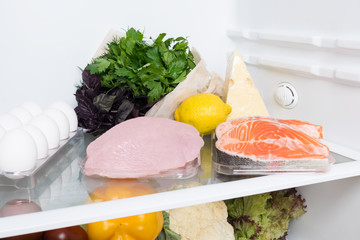 meat, fish and chicken with greens on a shelf in the refrigerator