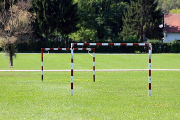 Red and white metal goal posts without back net mounted on local playground surrounded with green...