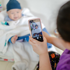 A photo of small baby sitting on the chair and his mother taking a photo of him