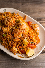 Stir fry Pad Thai with shrimp, squid, tofu, and peanuts. Served on a reclaimed wood table.