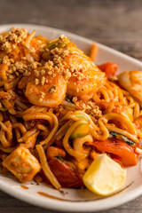 Stir fry Pad Thai with shrimp, squid, tofu, and peanuts. Served on a reclaimed wood table.