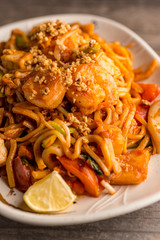 Stir fry Pad Thai with shrimp, squid, tofu, and peanuts. Served on a reclaimed wood table.