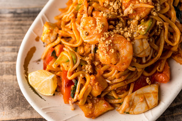 Stir fry Pad Thai with shrimp, squid, tofu, and peanuts. Served on a reclaimed wood table.