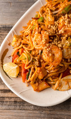 Stir fry Pad Thai with shrimp, squid, tofu, and peanuts. Served on a reclaimed wood table.
