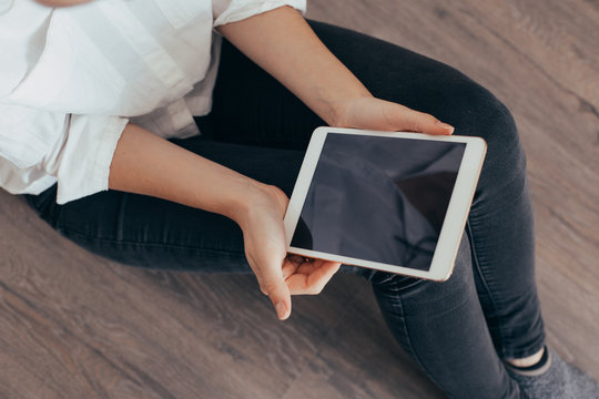 Mockup image of a woman sitting and holding white tablet pc with blank desktop screen