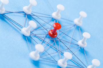 Obraz na płótnie Canvas network with red and white pins and string, An arrangement of colorful pins linked together with string on a blue background suggesting a network of connections.
