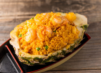 Malaysian Pineapple Shrimp Fried Rice with peas and cashew nuts. Served in a pineapple shell, plated in a boat, on reclaimed wood.