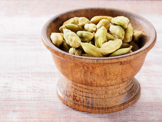 Spice Green cardamom (Elettaria cardamomum) in a wooden cup on a brown background