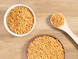 Fenugreek in clay plate, white bowl and spoon on a brown wooden background. Indian cuisine, ayurveda, naturopathy, modern apothecary concept