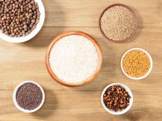 Rice, allspice, mustard seeds, fenugreek, cumin, cloves on brown wooden background. Indian cuisine, ayurveda, naturopathy, modern apothecary concept