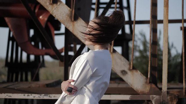 smart brunette woman in white with magnetic eyes poses against rusty seaport constructions closeup slow motion