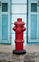 Fototapeta na wymiar Red fire hydrant at corner of walkway with background of light blue old Asian style door