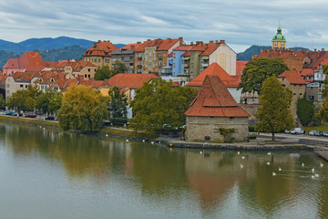 Fototapeta na wymiar Scenic autumn landscape of Drava River, embankment and Water Tower in Maribor. Cloudy morning, mountains at the background. Maribor, Slovenia