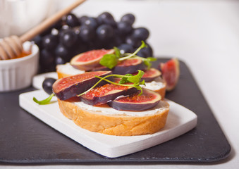 Sandwich with cream cheese, figs and honey served on a small white cutting board. Healthy food concept