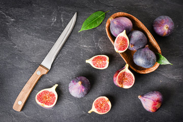 Fresh figs in wooden table on black background. Ripe citrus fig cut fruits on dark stone table from top view with knife.