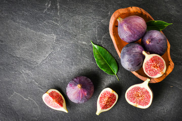 Fresh figs in rustic wood bowl top view. Cut fig fruit on dark stone table or black background with...