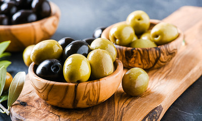 Fresh olives in bowl on dark stone table. Olive wood rustic board.