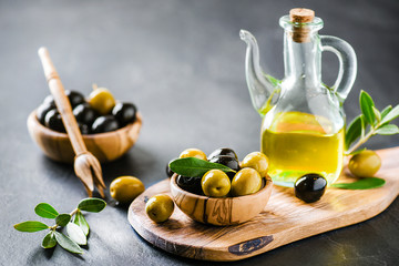 Ripe green and black olives on dark table with vigin oil in old glass bottle. Olive picker and...