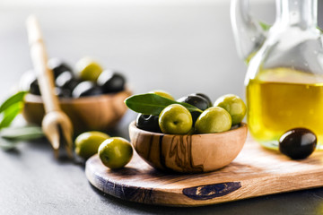 Ripe green and black olives on dark table with vigin oil in old glass bottle. Olive picker and...