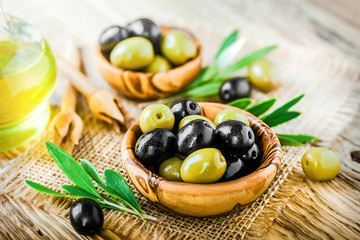 Fresh green and black olives in bowl on rustic old table. Olive oil on vintage board.